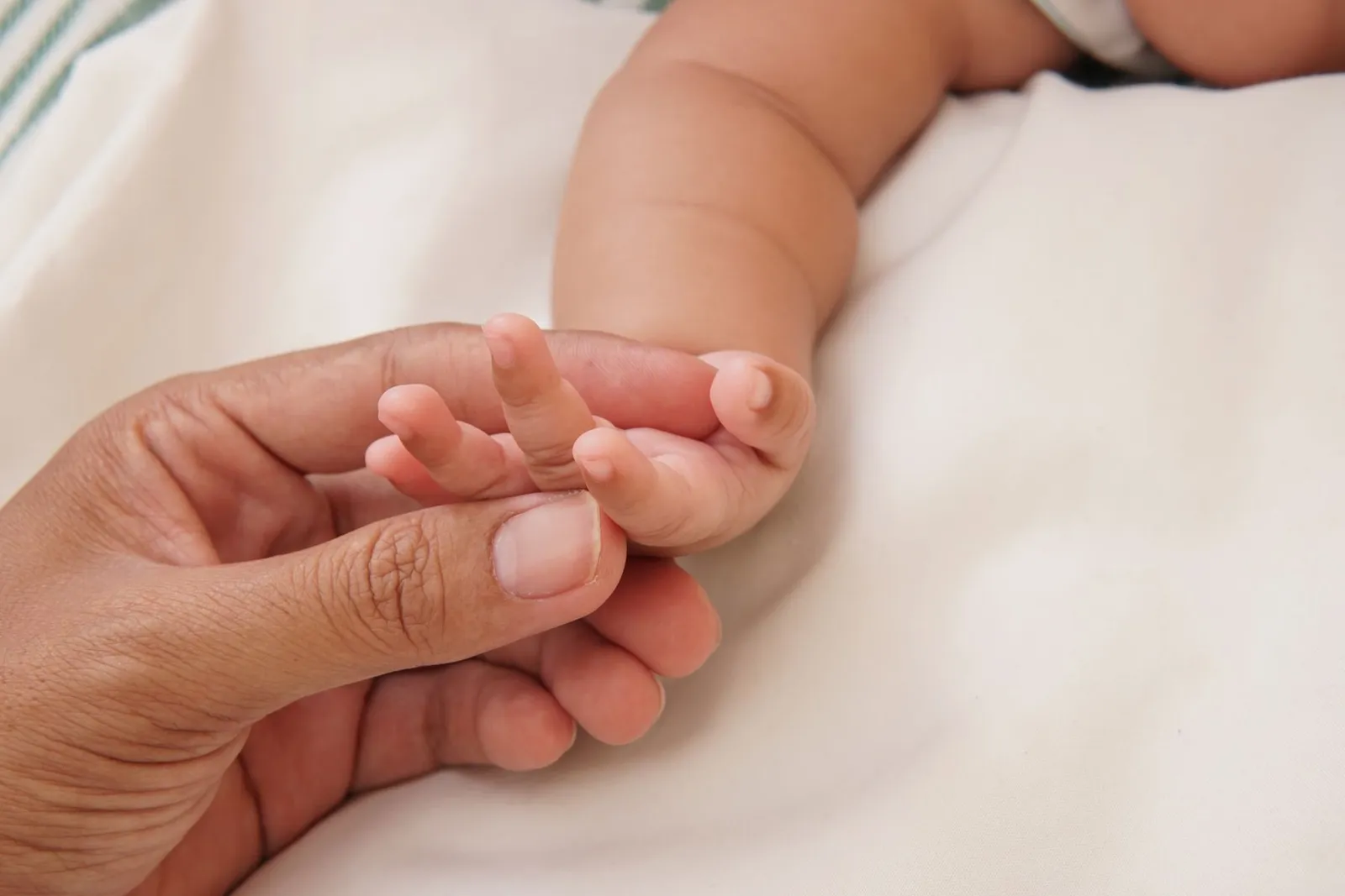 A parent's hand gently holding a newborn's fingers